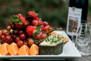 White serving tray piled with fresh grapefruit, strawberries, grapes and cheese next to a bottle of wine